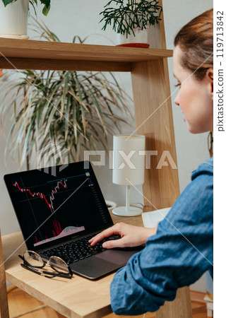 Tired woman is sitting her desk in home office, view from back. she looks at laptop screen with graph  119713842