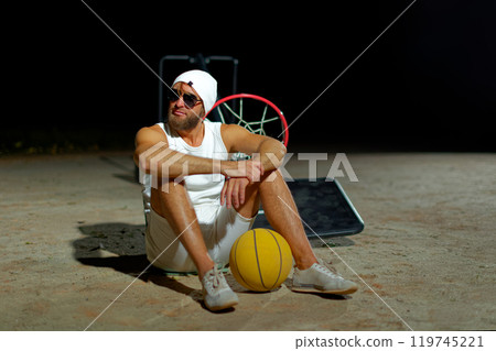 A basketball player sits on the court wearing sunglasses, relaxed after an intense practice session at dusk 119745221