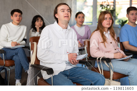 High school students sit at their desks and listen carefully to the teacher at lesson at school 119811603