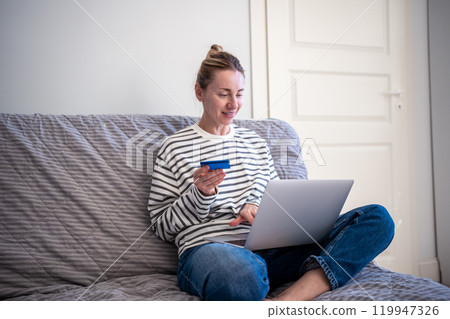 Happy woman resting on couch with laptop and credit card. Internet online shopping, home delivery. 119947326