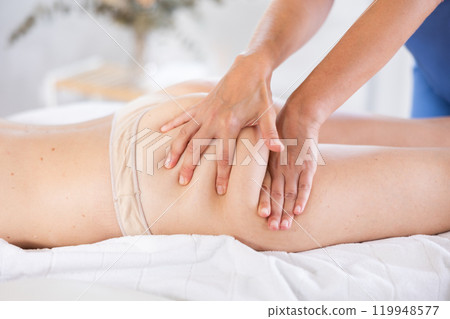 Professional masseuse doing anti-cellulite thigh and buttocks massage to woman 119948577