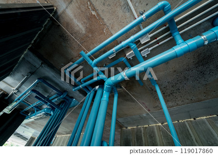 A bright blue pipes attached to a solid concrete wall 119017860