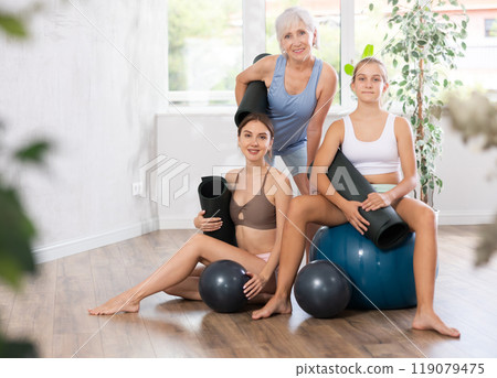 Three women of different ages in sportswear posing together in yoga studio 119079475