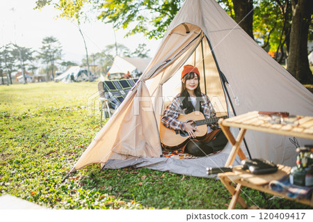 Woman playing guitar at campsite 120409417