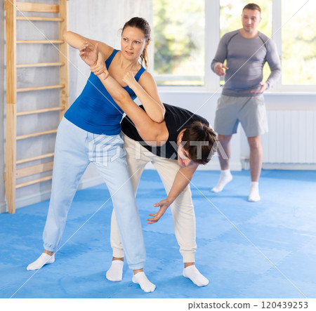 Woman training power move during self-defense training under guidance of trainer 120439253