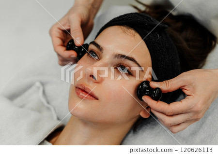 Woman receiving a facial treatment with massage tools in a serene setting 120626113