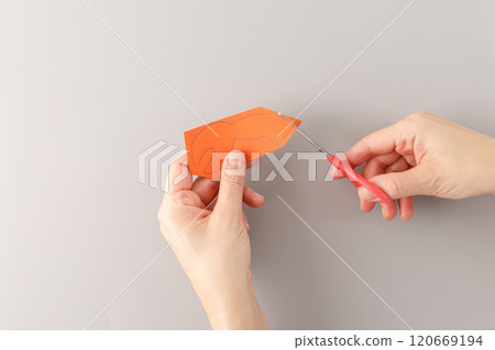 step in creative project, top down view one hand hold detail from carton and another hand hold red handle scissors which cutting out , claws made from orange paper, cut out details, grey background, 120669194