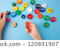 Childs hands arranging colorful bottle caps with multiplication problems on a blue background. Flat lay educational concept for learning and math games, 120891907