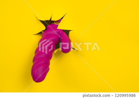 Magenta colored sex toy sticking out of yellow paper background. Copy space.  120995986