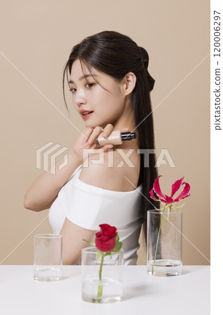 a woman in her 20s holding cosmetics in front of a table decorated with flowers 120006297