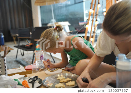 Mother and her daughter paint Halloween cookies  120037567