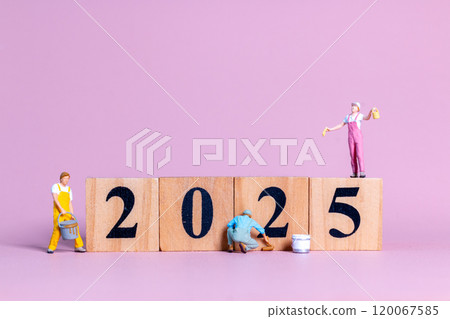 Miniature figures in overalls paint and construct the numbers "2025" on wooden blocks 120067585