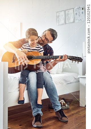 Teaching her about the different strings. Full length shot of a handsome mature man teaching his young daughter how to play the guitar. 120102941