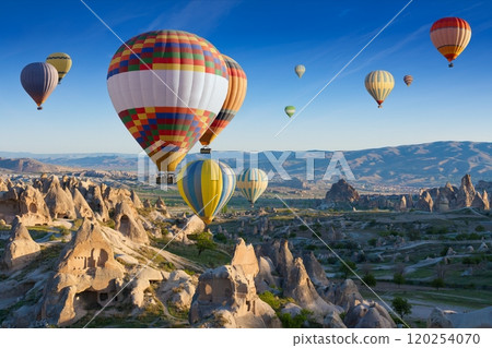 Colorful hot air balloons fly in blue sky over amazing rocky valley in Cappadocia, Turkey. 120254070