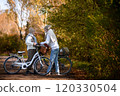 Elderly couple on walk in park, pushing their bikes side by side. Seniors in love on stroll through autumn city, enjoying a peaceful moment together. 120330504