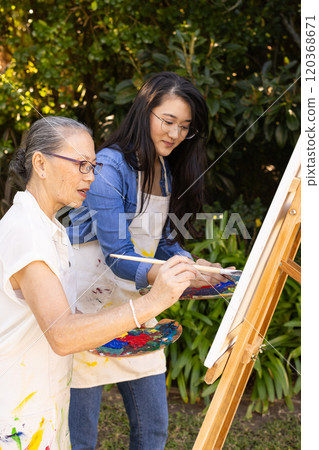 Painting on canvas, Asian granddaughter and grandmother enjoying outdoor art activity together 120368671