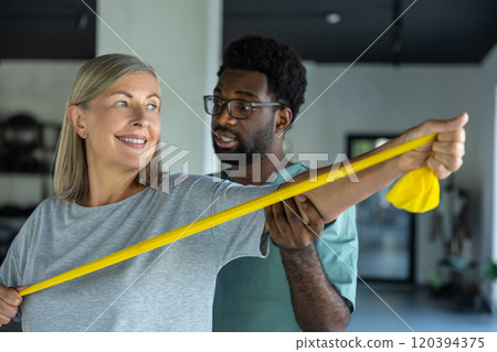 Female patient working with stretching band, male doctor helping her 120394375