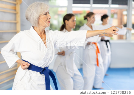 Women of different ages in kimono standing in fight stance during group karate training in gym 121738256