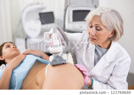 Old woman specialist doing LPG massage of hips of young woman 121768680