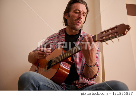 Man playing acoustic guitar indoors in a casual and relaxed environment 121855857