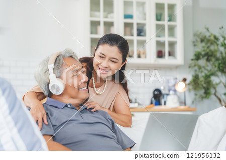 Senior spouses using laptop together sitting on couch at home 121956132