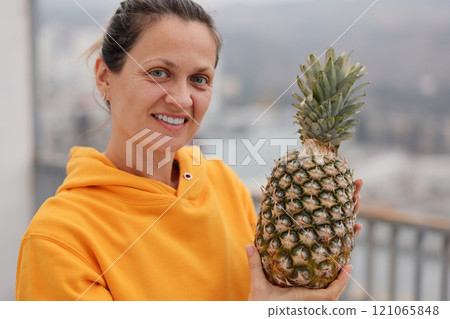 A Cheerful Woman Holding a Pineapple While Enjoying an Urban Setting Full of Life 121065848