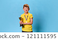 Portrait of little boy with patch on hand, posing grimacing and holding golden cup after vaccination against pastel blue background. 121111595