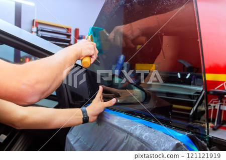 Technician carefully applied window tint film to car in an auto shop, ensuring precise alignment, quality finish. 121121919