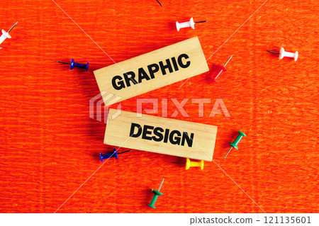 Wooden blocks spelling graphic design placed on a vibrant orange background with colorful push pins scattered around 121135601