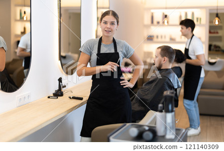 Girl hairdresser stylist stands near workplace with tool in hands. 121140309