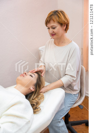 Healer woman performing set of 32 points of access bars on young woman head, stimulating positive change thoughts and emotions. Alternative medicine concept 121211478