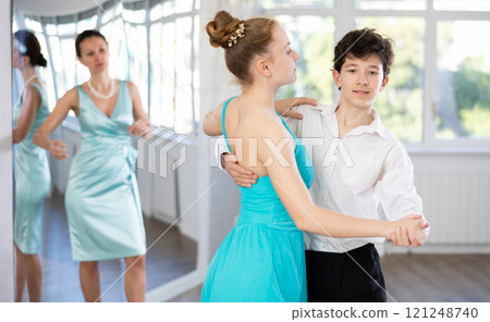 Experienced female dancer teaches tango to pair of teenagers in ballroom 121248740