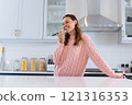 Smiling woman in kitchen singing into microphone, enjoying festive moment, at home 121316353