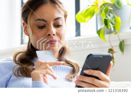 At home, woman shopping online with credit card and smartphone, looking focused 121316392