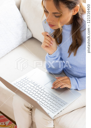 Woman shopping online using laptop and credit card at home, looking thoughtful 121316400