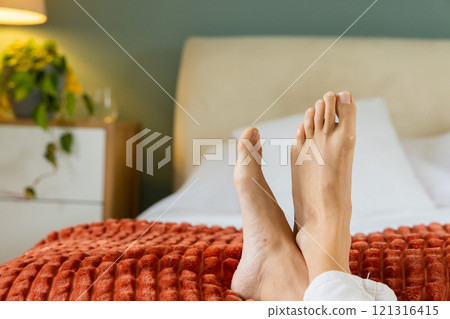 Relaxing at home, woman resting feet on cozy bed with red blanket 121316415