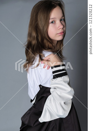 A girl turns slightly, looking thoughtfully to the side, her jacket resting on her shoulder. This portrait expresses the blend of innocence and emerging maturity seen in adolescence. 121328212