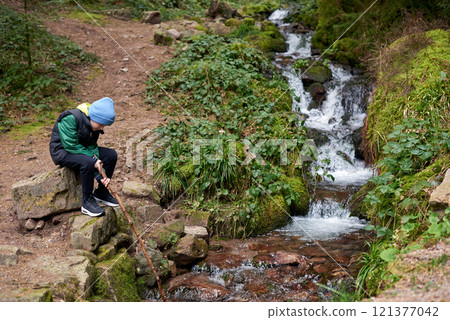 Children hiking in Alps mountains crossing river. Kids play in water at mountain in Austria. Spring family vacation. Little boy on hike trail. Outdoor fun. Active recreation with children. 121377042