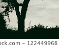 Silhouette of a a tree against a grey sky with space for text. Contrasting dark tree growing in a clearing with grass and flowers in bloom in summer.  122449968