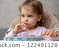 A thoughtful toddler sitting at the table, observing her surroundings in a cozy home setting 122481128