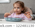 A playful toddler sitting at the table with a curious expression in a cozy home setting 122481130