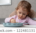 A curious toddler exploring her meal while sitting at the table in a cozy home setting 122481131