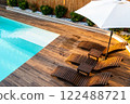 Luxury poolside wooden deck with modern lounge chairs, umbrella, and turquoise swimming pool 122488721