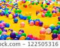 A vibrant scene of colorful plastic balls scattered across a bright yellow play surface. 122505316