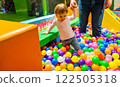 Toddler playing in a colorful ball pit with supportive adult guidance. 122505318