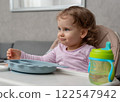 A curious toddler enjoying mealtime with a sippy cup and playful expression. 122547942