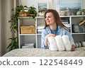 Modern housewife putting neatly folded towels, pillowcases, duvet covers into wicker natural basket 122548449