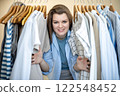 Smiling brunette beautiful woman choosing clothes neutral cotton beige textile on rack 122548452