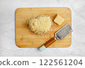 Grated cheese and block of cheese on a wooden cutting board in a kitchen 122561204