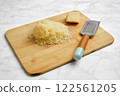 Shredded cheese on wooden cutting board with grater and cheese block 122561205